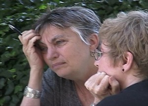 Color photograph of the heads of two women in thoughtful poses, each resting her heads on one of their hands. The gray haired woman holds a pen between her fingers and wears a silver bracelet, the brown haired women wears eyeglasses. From "Vigil," the short film by Mignon & Wolf Naegeli about Women in Black Knoxville.